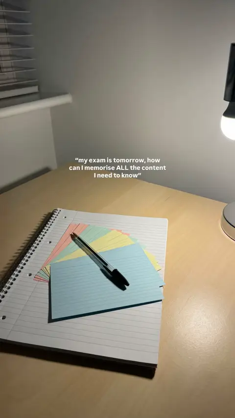 A desk with a notepad, index cards, and a pen is lit by soft light from a lamp. The image has a muted color palette with a warm, inviting tone.