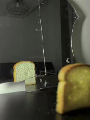 A close-up shot features two slices of toasted bread. One piece is mostly in focus, with a yellow-brown crust and a soft, textured interior. Next to it, the broken mirror shows its reflection. The scene is dimly lit with a dark background.