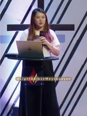 The image shows a woman standing behind a podium with a laptop, speaking into a microphone. She is facing the camera. There's a cross decoration on the background. The background is blue with white stripes. Text overlays include a username and a quote from her.