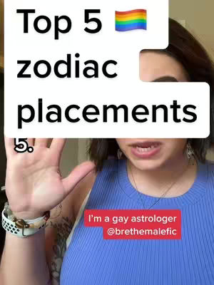 A woman with dark hair and a blue top is centered in the frame, her face partially visible. A large white rectangle overlays the top half of the image, displaying the text 'Top 5 zodiac placements' in a bold font. A rainbow flag is in the top right corner. The woman's hand is up with fingers spread. A smaller red rectangle at the bottom displays text identifying the creator as a gay astrologer.