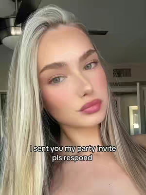 A selfie-style shot featuring a young woman with long, wavy blonde-highlighted hair. She faces the camera, with soft lighting illuminating her face and shoulders. The image includes a visible ceiling fan in the background and text overlayed. The focus is clearly on the subject's face.