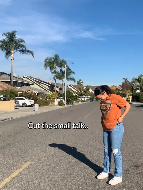 The cover image shows a woman in jeans and an orange t-shirt standing on a road. She has dark hair and is wearing glasses. The background includes a blue sky, houses, and palm trees. Text overlayed at the bottom reads, 'Cut the small talk..'