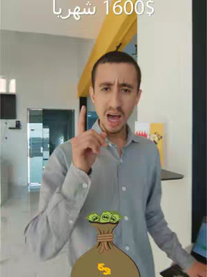 A man with short dark hair, wearing a gray button-down shirt, is pointing upwards with his right index finger. The image appears to be taken in a bright indoor setting, possibly an office or home entrance area. A cartoon money bag with the dollar sign is added at the bottom. Text in Arabic is placed above the man's head.