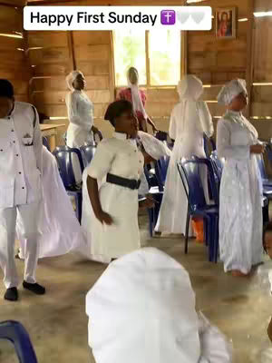 The video shows a well-lit interior church scene with several people in white garments. A text overlay reads 'Happy First Sunday'. The layout includes blue chairs, a window in the background, and a framed image on the wall.