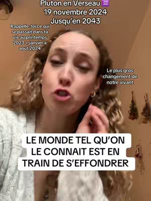 The cover image presents a woman with fair skin, curly brown hair, and a neutral expression, positioned in a medium shot with the image's focus centered on her face. She is in a light-colored top. Text overlays are present, including a title at the top in a sans-serif font that reads 'Pluton en Verseau' with subtitle information directly below in a similar font, indicating the transition of a planet into the sign of Aquarius. Further below the title, there is a text block with more details and a bottom section written in a white rectangle which reads, 'LE MONDE TEL QU'ON LE CONNAIT EST EN TRAIN DE S'EFFONDRER'. The background is soft-lit.