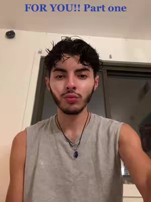 A man with dark hair and a short beard is centered in front of a plain background. The text 'FOR YOU!! Part one' is in blue at the top of the image. He's wearing a sleeveless gray shirt and a necklace with a small blue/purple pendant.