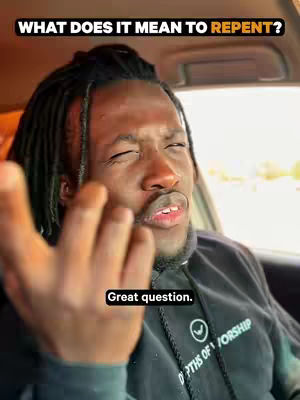 A close-up shot of a Black man in a car, with a questioning expression. The video includes overlaid text and the man's hand is raised, likely indicating he is speaking. The background is blurred, but appears to be a road.
