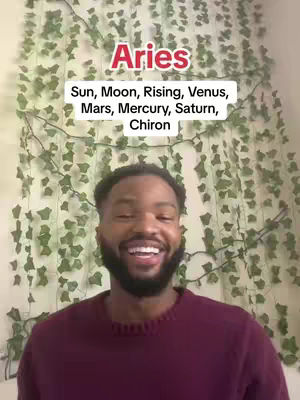 A man with a beard smiles at the camera. Behind him is a wall covered in fake vines. Text overlays read "Aries" and a list of astrological terms.