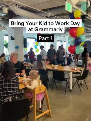The cover image shows a brightly lit office space bustling with people, including adults and children, suggesting a family-friendly work environment. A highchair with a child seated at a table is in the foreground. Balloons in various colors are clustered together, contributing to the festive atmosphere.