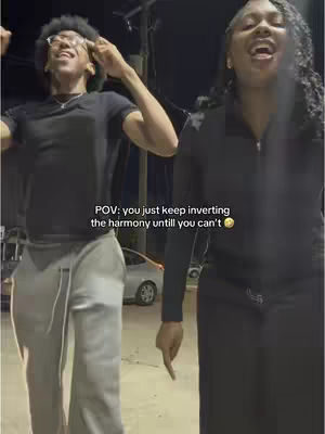 Two young people, a man and a woman, are standing outdoors at night under artificial lighting, likely in front of a building. The man is on the left and the woman on the right. They are both smiling and singing, with the man gesturing upwards with his right hand and pointing with his left. The woman holds her right arm slightly bent. A car is visible in the background. The hook text appears in the middle.