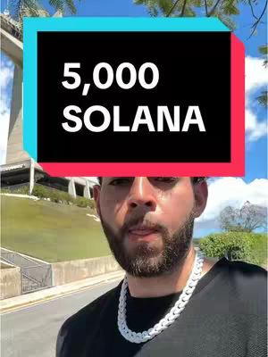 A man with a beard and a white chain necklace stands outside on a sunny day. A text overlay in a brightly colored box covers the top of the frame.