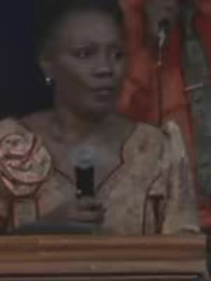 The cover image shows a woman speaking into a microphone. She has short hair and is wearing a beige top and dark jacket. The background is out-of-focus, possibly a stage or auditorium setting.