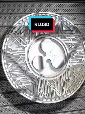 A silver coin-like object with a central ripple logo, overlaid with a black and colored text bar that reads "RLUSD", set against a background of what appears to be a metal surface with a grid pattern.