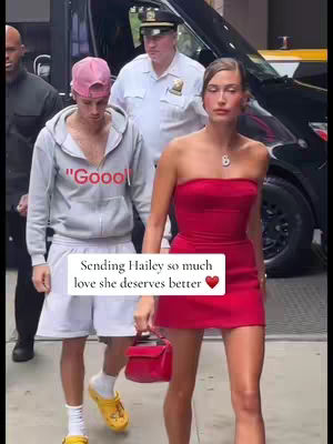 The image shows a street scene with a man and a woman walking side by side, and 3 other people or figures in the background. The man, wearing a pink cap, and a gray hoodie with a word on it,  is walking next to a woman wearing a red dress, in a formal setting. There is also a white rectangle in the image with text on it.
