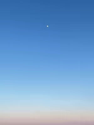 A photograph of a clear blue sky with a faded pink and pale color at the bottom. A small bright dot is visible in the center of the sky.