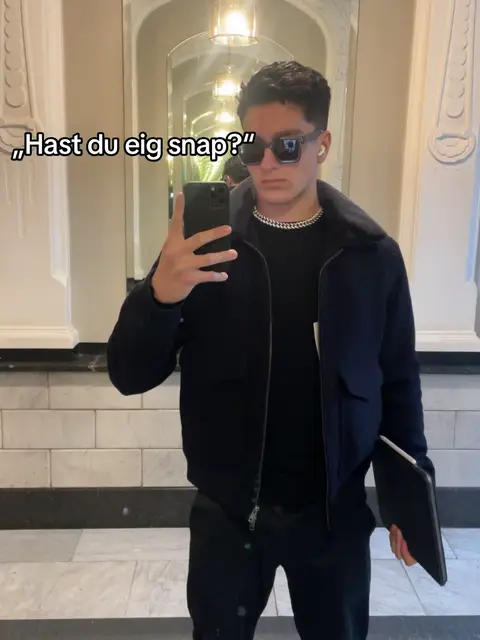 A man in a black jacket, black pants, and sunglasses poses in front of a mirror. Text overlays the image.