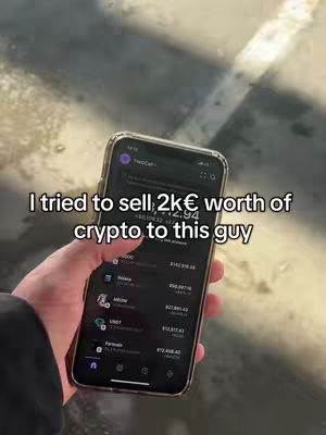 A hand holding a smartphone with a black screen displaying a crypto app, set against a blurred outdoor background with sunlight.