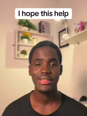 A medium shot shows a young Black man looking at the camera with a slightly open mouth, as if about to speak. Above his head, a white rectangular text box reads 'I hope this help'. The background is somewhat blurred, featuring a shelf with plants and other objects. The lighting seems to be daylight or bright indoor lighting.