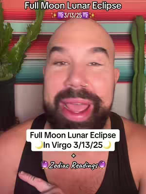 A man with a beard and a bald head is looking at the camera with an open mouth. Text overlays on the image announce the upcoming full moon lunar eclipse in Virgo, with a date, and a reference to zodiac readings. Colorful striped fabric is in the background, with green plants on either side of the man.