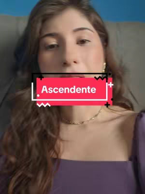 A woman with long, wavy brown hair is centered in a selfie-style shot. The background is a blurred dark shade. She wears a purple top and a gold chain. A red rectangle with white text reading 'Ascendente' is overlaid on her face.