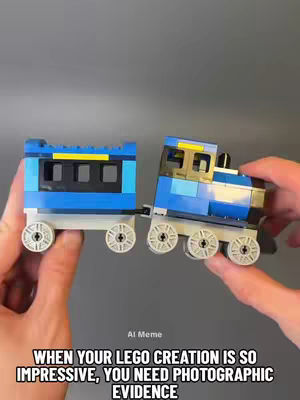 A person's hands holding a blue and grey toy train. The train is made of Lego blocks. The background is a plain grey.