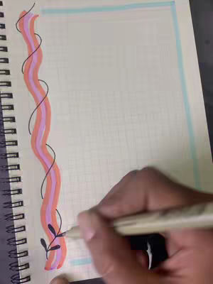 A hand is drawing on a gridded notebook. The notebook is open, revealing a page with a colorful border. The border consists of a wavy, vertical stripe colored with pink, orange, and yellow. The hand, holding a pen, is sketching a small leaf design off the side of the border. The background is a muted beige.