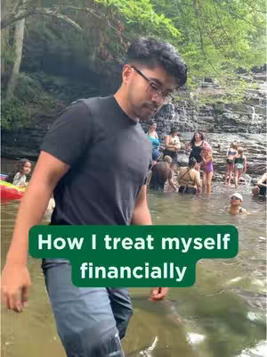 A man in a black t-shirt and glasses stands in a river or stream, with other people in the water and a rocky background with trees. A green banner at the bottom reads 'How I treat myself financially'.