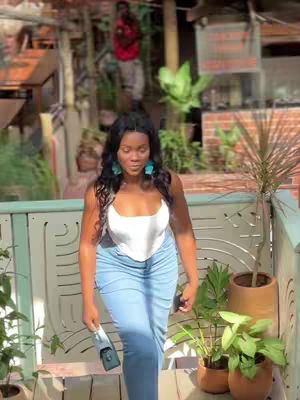A woman in a white top and blue jeans stands on a wooden patio with a green railing and plants in the background .