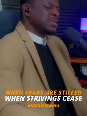 A man with short dark hair wearing a tan blazer over a black sweater is singing into a microphone. The background is dark with what appears to be sound-proofing. Text overlays read 'WHEN FEARS ARE STILLED WHEN STRIVINGS CEASE @danieltww'.