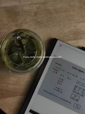 The cover image shows a top-down view of a wooden table. On the table, there's a clear glass with green liquid and a straw, likely containing matcha or a similar drink. To the right, a digital tablet displays what looks like a math problem. The text overlay says, "if you really really dedicate yourself."