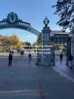 The cover image shows a wide shot of a university campus entrance. A large, ornate archway of metal and stone is in the midground, with the university's name or logo subtly etched at the top. People are walking on the paved path leading towards the entrance. The sky is clear with a few trees in the background.
