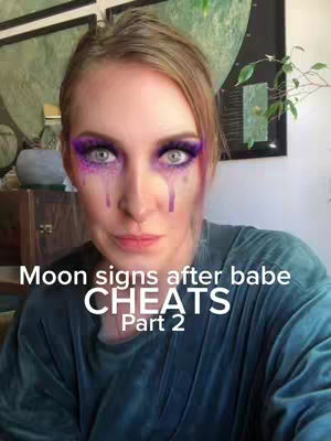 A selfie-style video cover featuring a woman with blonde hair and purple eyeshadow, appearing to cry but with the tears being streaks of purple makeup. The text overlay is in white font and reads 'Moon signs after babe CHEATS Part 2.' The background is a minimalist interior with framed artwork and plant.