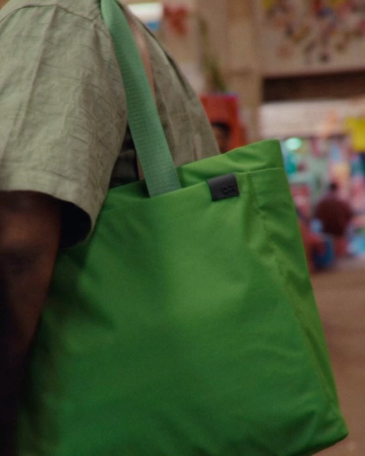 The cover image shows a person from the shoulders up, holding a bright green tote bag. The person is wearing a light green shirt and the bag’s strap is also green. The background is blurred, suggesting an outdoor or market setting.