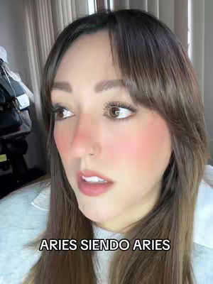 The cover image shows a close-up of a woman's face angled slightly to the side, with a soft background. She has brown hair with bangs, light skin which is blushed. The text overlayed at the bottom states 'ARIES SIENDO ARIES'.