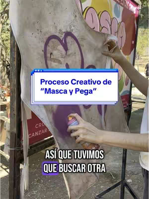 The image shows a close-up view of a creative process. A person's hand is visible, holding a spray paint can and spraying a purple color onto a large, off-white canvas that is hanging. The canvas appears to have a graffiti-style design partly visible. Overlaid on the image are two text boxes providing context. The background is somewhat blurred, but includes elements of what looks like an urban or outdoor setting.