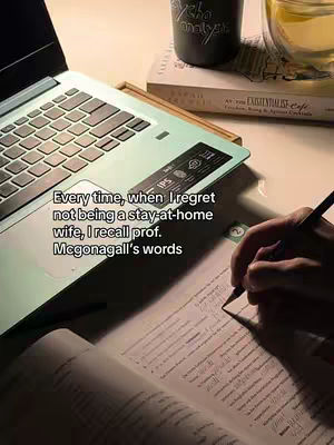 A close-up, slightly above view of a workspace featuring a laptop, a book, a mug, and a glass of tea. The laptop is open, displaying its keyboard and a label. A hand is visible, holding a pen and writing on a textbook. The image has a warm, soft lighting.