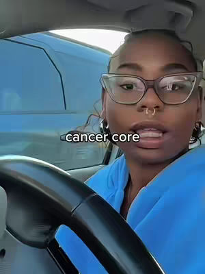 A woman with glasses and a nose ring is in a car, looking at the camera. The text overlay reads "cancer core".