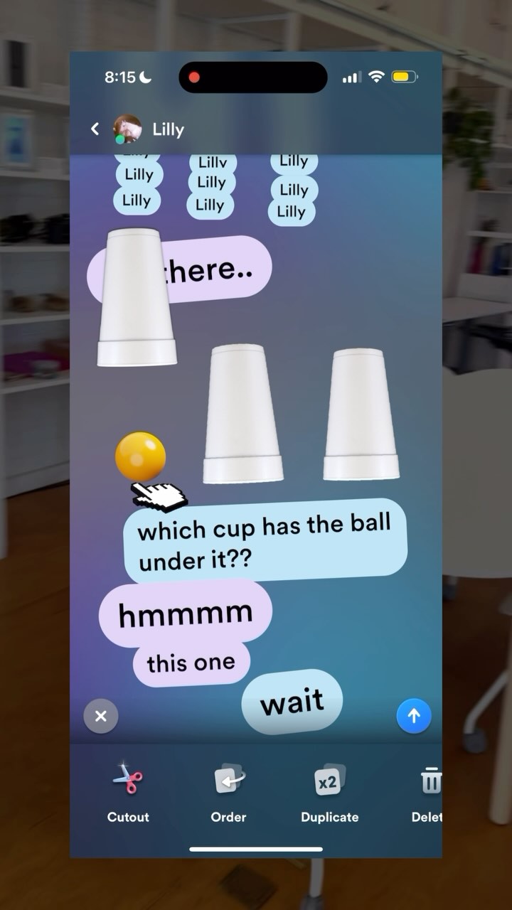The image shows a mobile screen with a game-like interface. The upper part features the time and notifications. Below, there's a chat interface with multiple 'Lilly' bubbles. Three white cups are displayed, and a yellow ball with a hand cursor on the left of the cups. The dialogue bubbles discuss the ball's location under a cup. The interface includes editing options at the bottom.