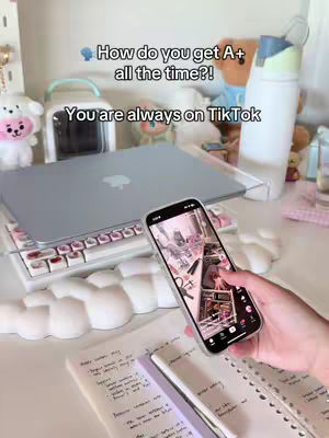 The cover image shows a desk setup. A laptop is open on a laptop stand, with a white keyboard in front of it. To the right, is a water bottle. In the user's hand is a phone displaying a TikTok video, and a notebook and pen are below it. On the left, a white plushy is placed among desk accessories. The text overlay is in a clear format.