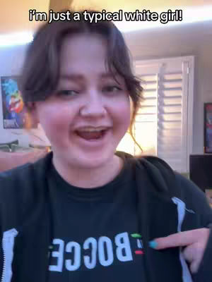 A young woman with dark hair and a black zip-up hoodie is shown smiling and pointing. Above her is the text overlay, "I'm just a typical white girl!"