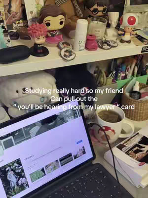 A cluttered desk setup features a laptop displaying a website, a mug of tea, and various decorative items on a shelf in the background. The color palette is muted, with the focus on the desk and its contents. There is text overlayed toward the bottom part of the image