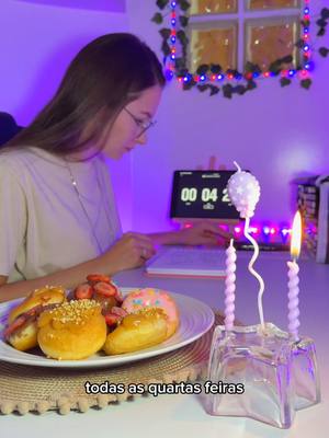 A woman is seated at a desk with a laptop and a plate of food. In front of her is a plate of pastries and fruit, and behind them, two lit candles add a celebratory vibe to the scene. The background is a soft purple, enhancing the video's relaxing atmosphere.