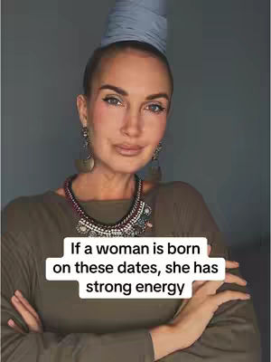 A woman with a stylized, tall head covering and ornate jewelry is the central focus, set against a plain background. She is wearing a long-sleeved olive green top and has her arms crossed. A text overlay in a white box at the bottom of the frame reads, “If a woman is born on these dates, she has strong energy.”