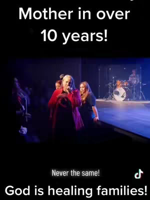 The cover image shows a live event with a woman speaking into a microphone on a stage, with other people and musical instruments in the background. Text overlays state the woman was a mother for over 10 years, with a concluding message that God is healing families.