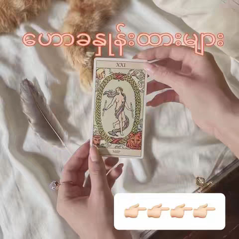 A person's hands holding a tarot card depicting a woman within a golden oval, with hands around the card and a white sheet background with a feather.