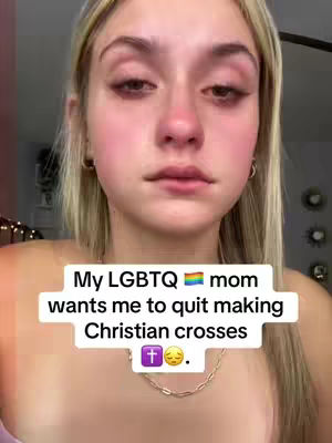 A close-up shot of a young woman with blonde hair and pale skin. She is looking down with a sorrowful expression. A text overlay reads, "My LGBTQ mom wants me to quit making Christian crosses," with a cross and crying emoji.
