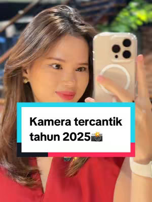 A young woman is taking a selfie with a smartphone. The woman has long, brown hair and is wearing a red top. She is holding the phone up with her right hand, with a visible phone case. A text overlay is visible on the bottom of the frame.