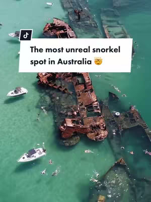 Aerial view of turquoise water with several partially submerged shipwrecks, with small boats and people snorkeling around them.