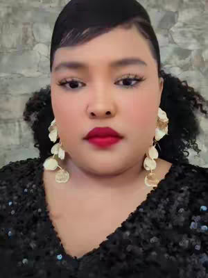 The cover image features a close-up of a woman. She has a fair complexion, dark hair, and is wearing a black sequined top. Her red lipstick and large gold earrings are also visible.