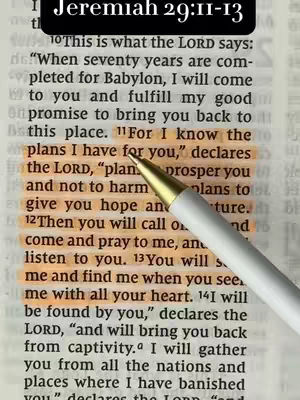 The image is a close-up of a page from the Bible, with a pen resting on it. The text on the page is from Jeremiah 29:11-13, highlighted in orange. The background is a slightly yellowed paper with a very high density. The pen is white with a gold tip.